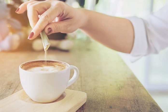 Closeup of lady pouring sugar while preparing hot coffee cup